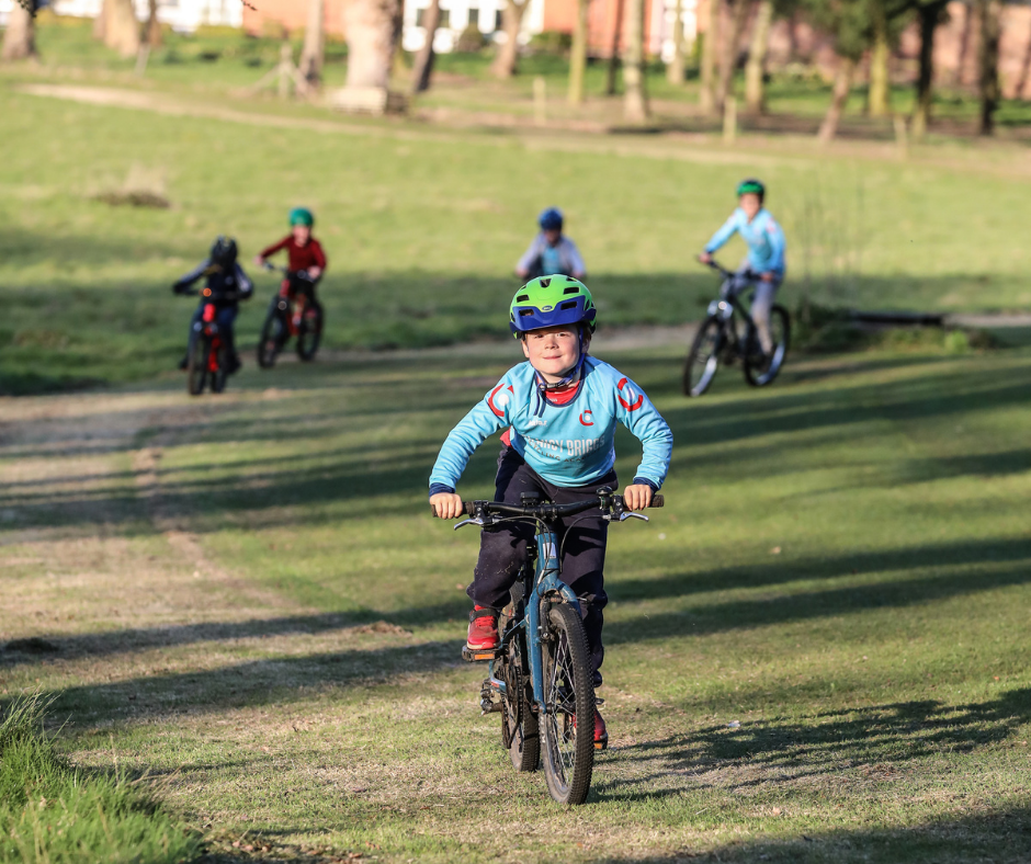 Young riders in our Pedal class cycling up a grassy hill.